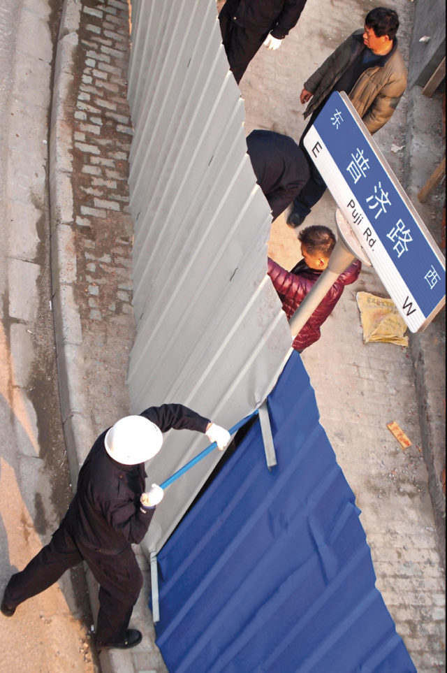 Chengguan officers busy taking down the fence around an illegal construction before demolition, while being filmed by local TV, in Zhabei district, Shanghai, 29 January 2013. Photo: Remko Tanis