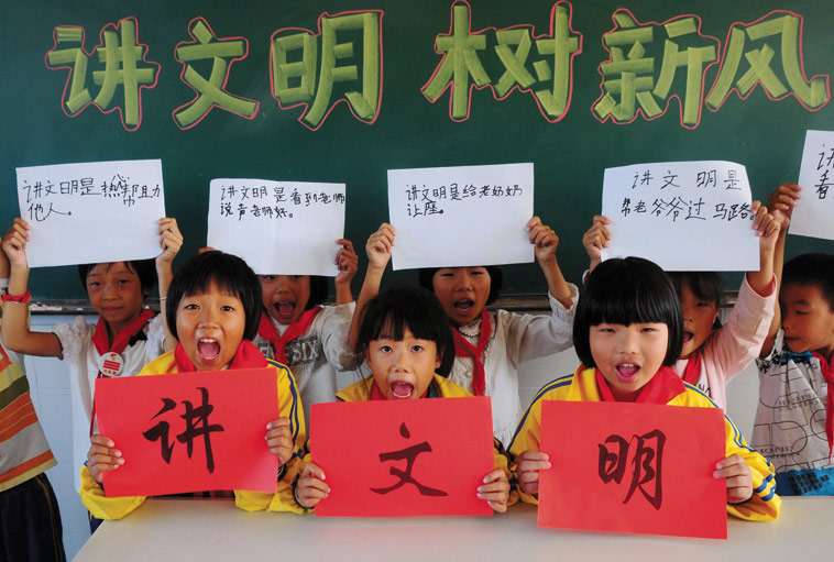 Primary school students during a class exercise on how to be civilised (jiang wenming 讲文明). The students in the back row hold signs that say being civilised means helping other people, giving up your seat for seniors and helping the elderly cross the street. Source: ImagineChina